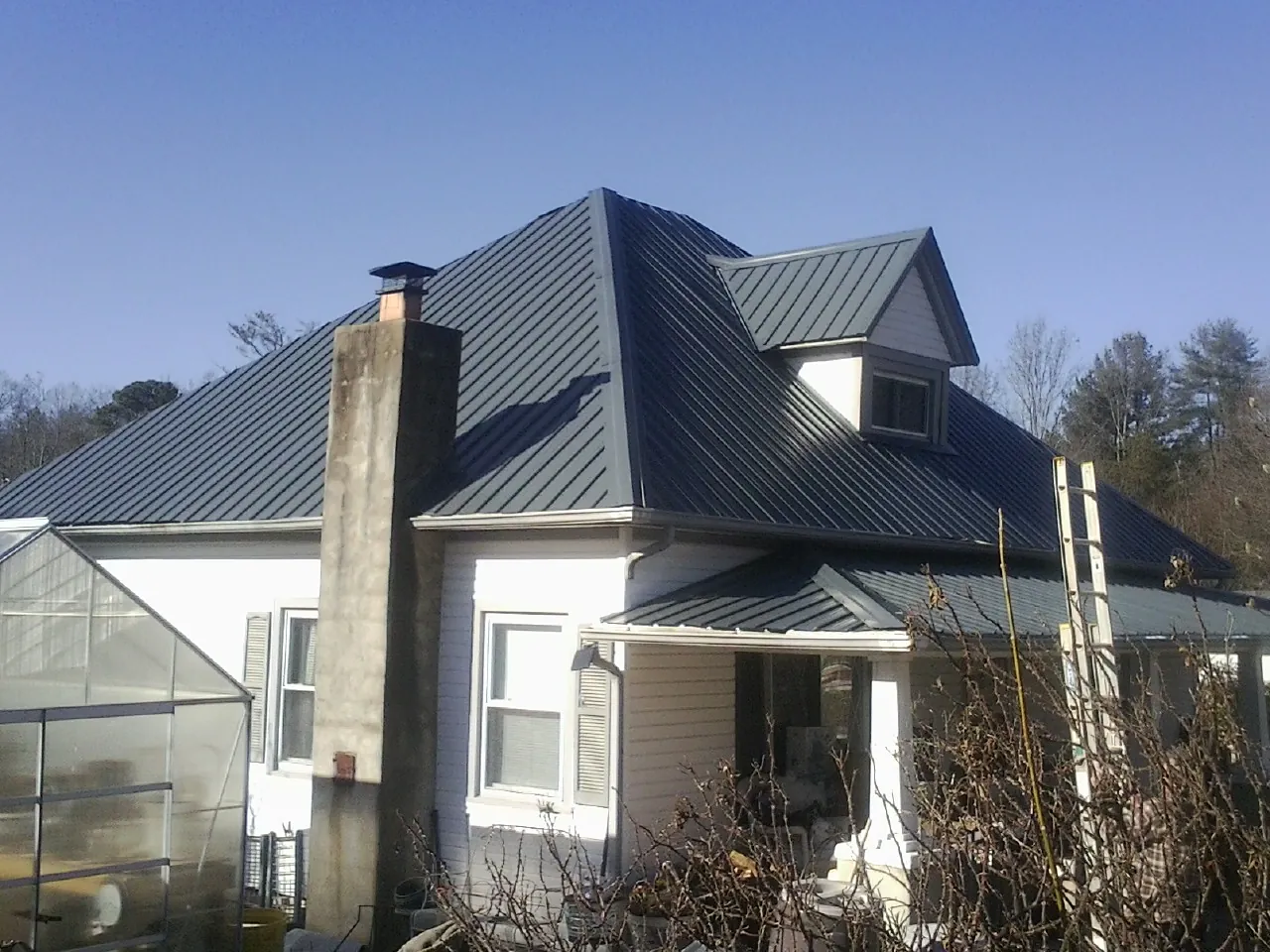 Dark blue standing seam metal roof on a white farmhouse with dormer — Slate & Tile Roof Repair by Roofing Brothers in Dahlgren