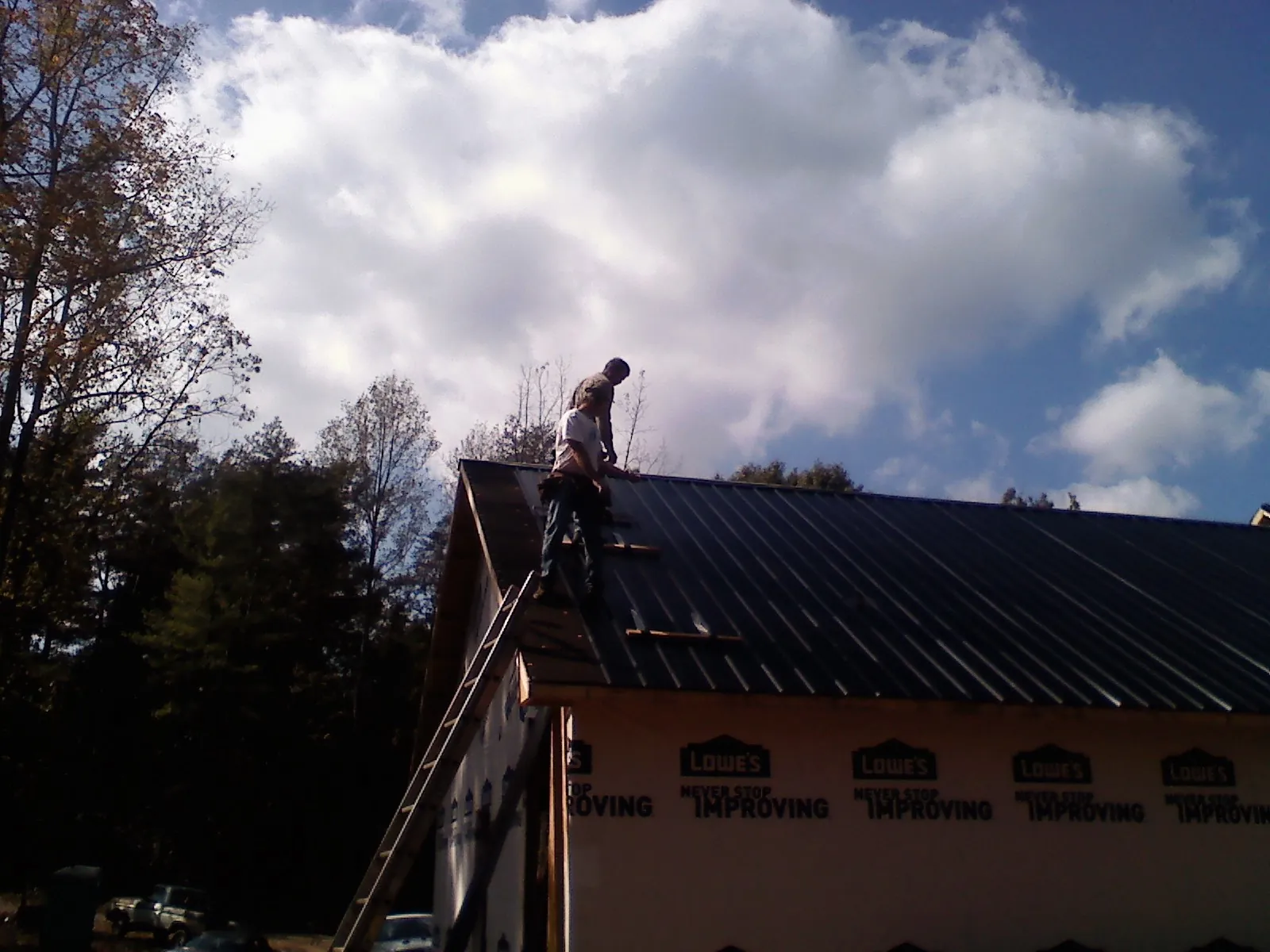 Roofer fastening dark metal panels high against a cloudy sky, from a Roof Inspection job in Dahlgren
